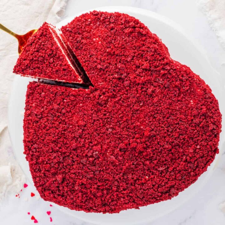 A red velvet cake in the shape of a heart on a white plate.