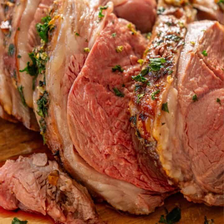 A seared leg of lamb roast is sitting on a wooden cutting board.