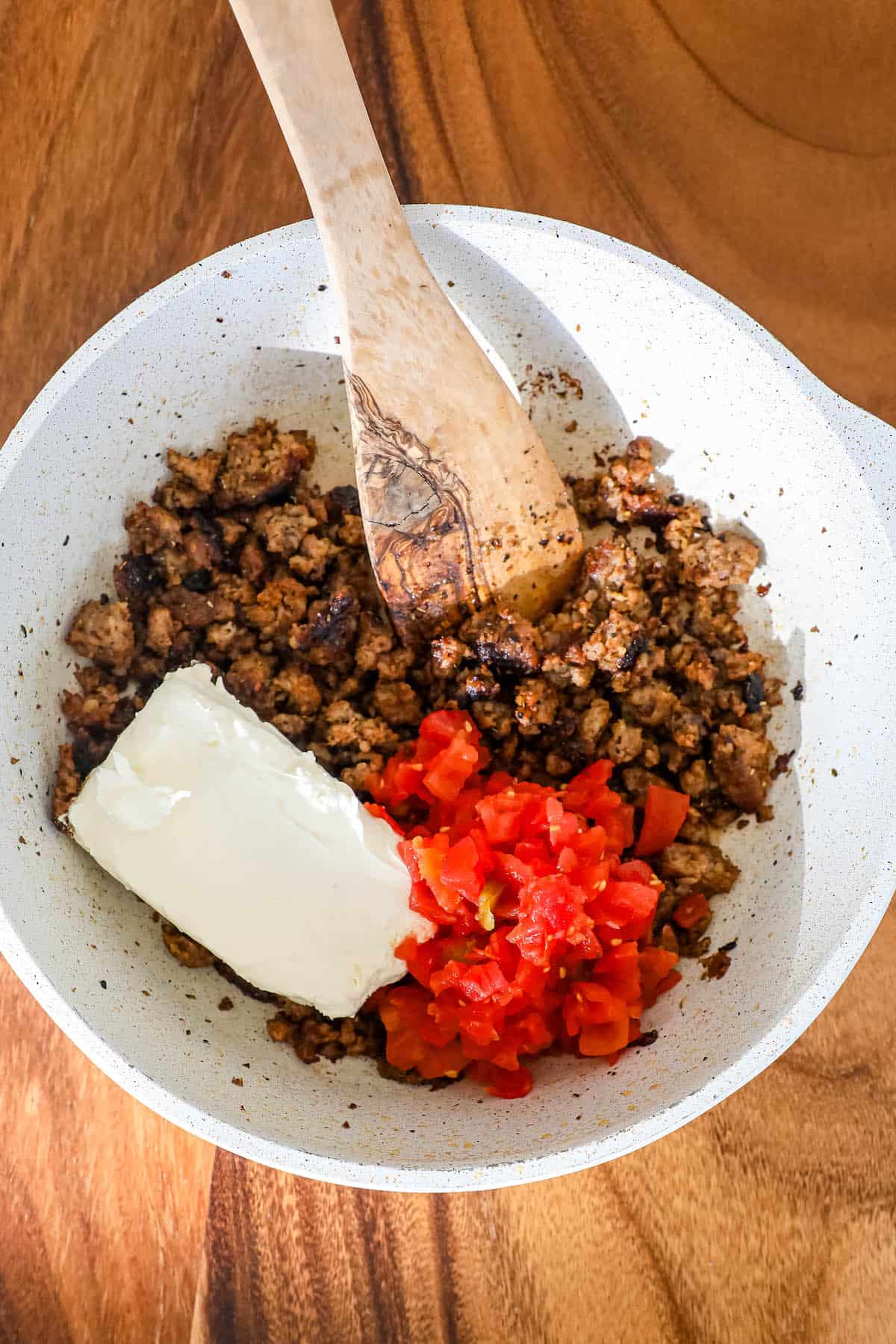 A white bowl filled with meat, tomatoes, and butter.