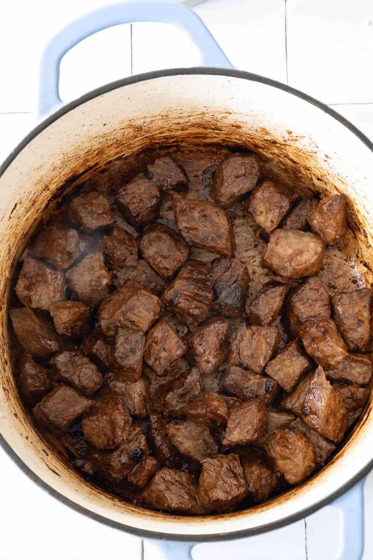 A spicy beef stew simmering in a pot on a tiled floor.