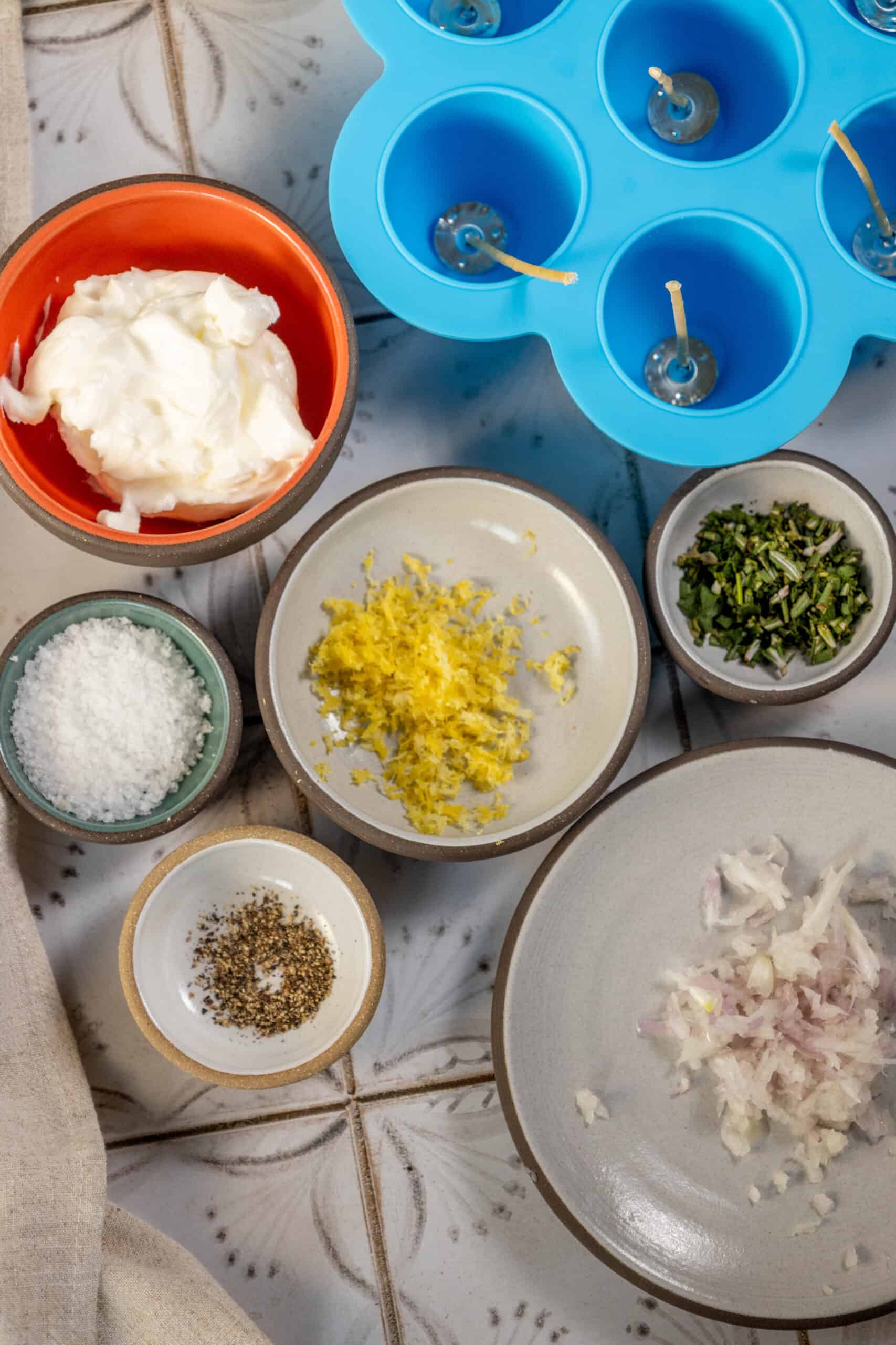 A bowl of onions, garlic, and other ingredients illuminated by candles on a tiled floor.