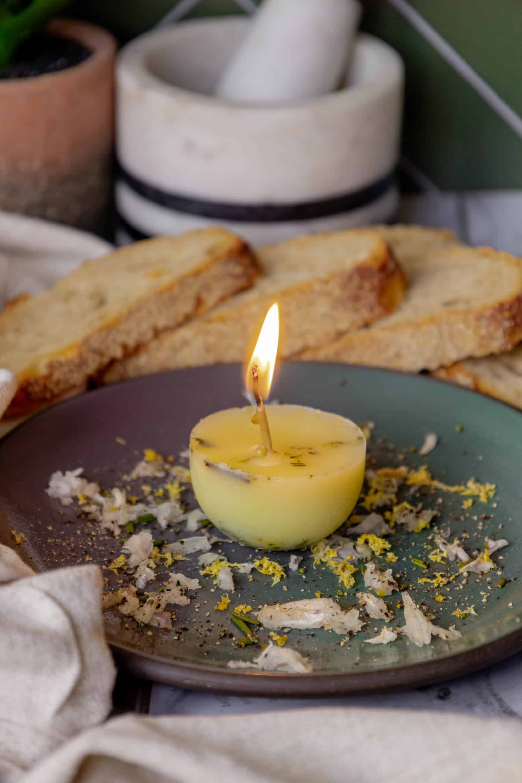 In this scene, a tallow candle is sitting on a plate next to some bread.