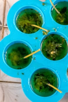 A tray filled with ice cubes filled with green liquid, surrounded by flickering tallow candles.