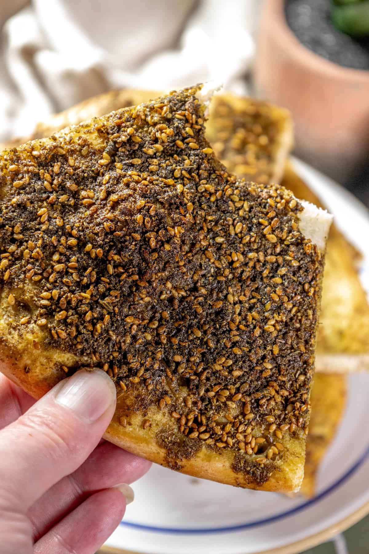 A person holding a piece of bread with Za'atar sprinkled on it.