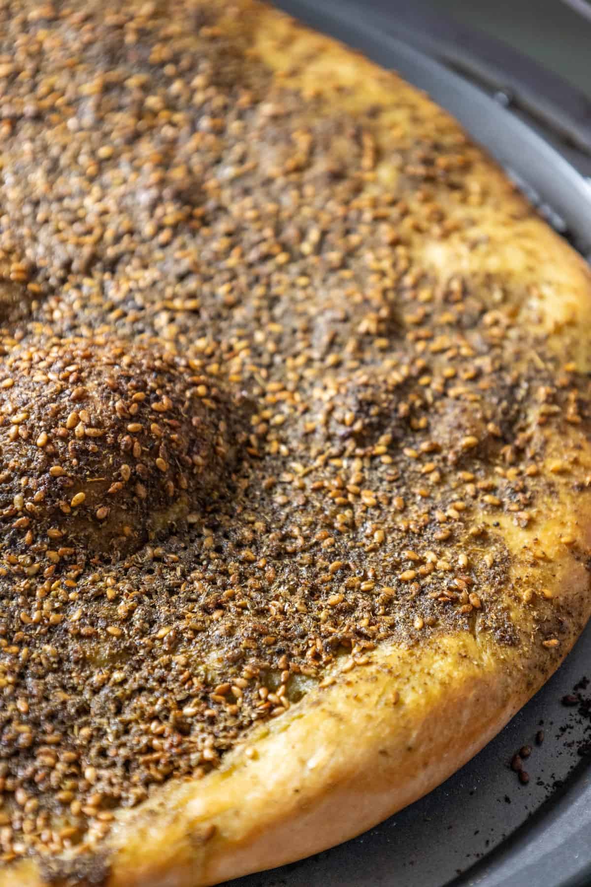 A Za'atar pizza, also known as za'atar manakish, is sitting on a pan with seeds on it.