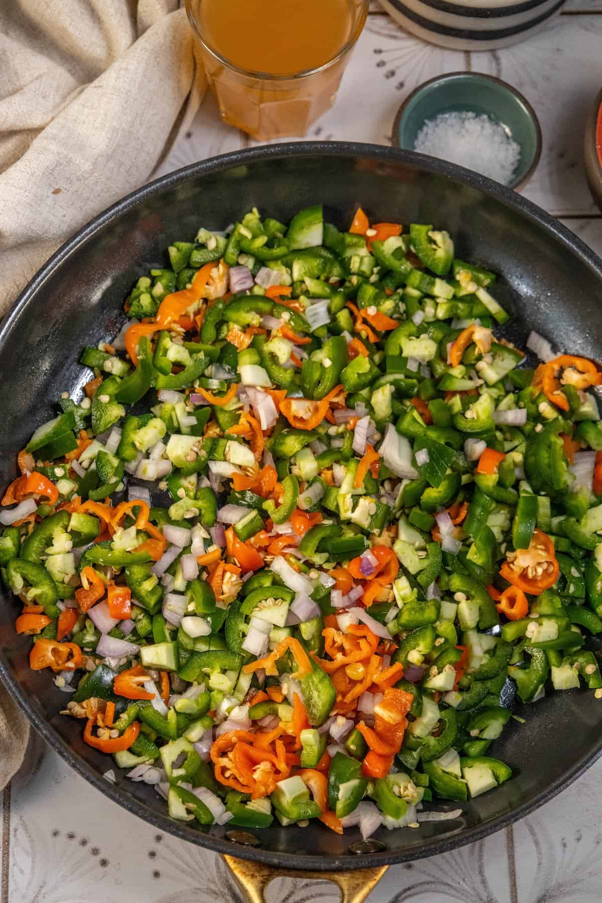A frying pan with vegetables in it, enhanced with a hint of hot sauce.
