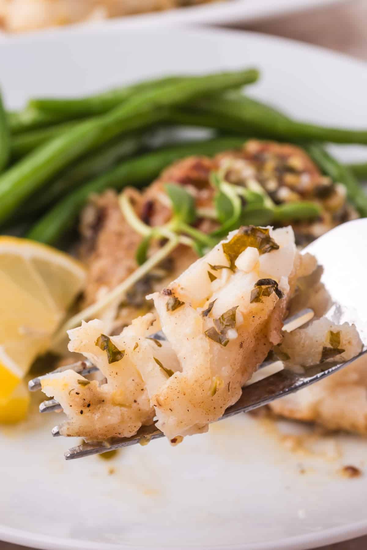 A fork is holding a piece of pan-fried cod and green beans in this seafood dish.