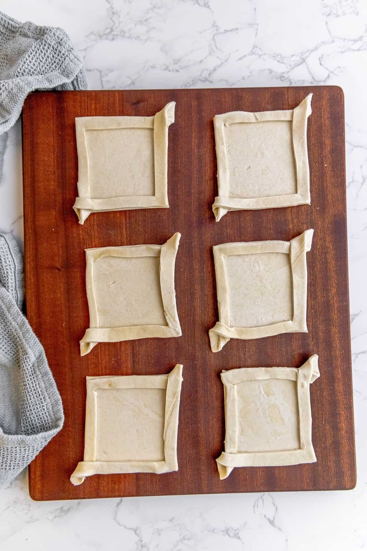 A square shaped dough on a wooden board.