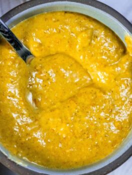 A bowl of yellow sauce with a spoon in it.