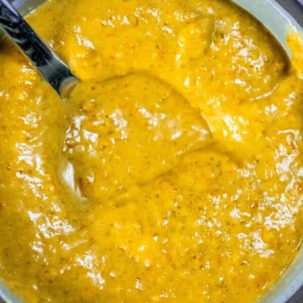 A bowl of yellow sauce with a spoon in it.