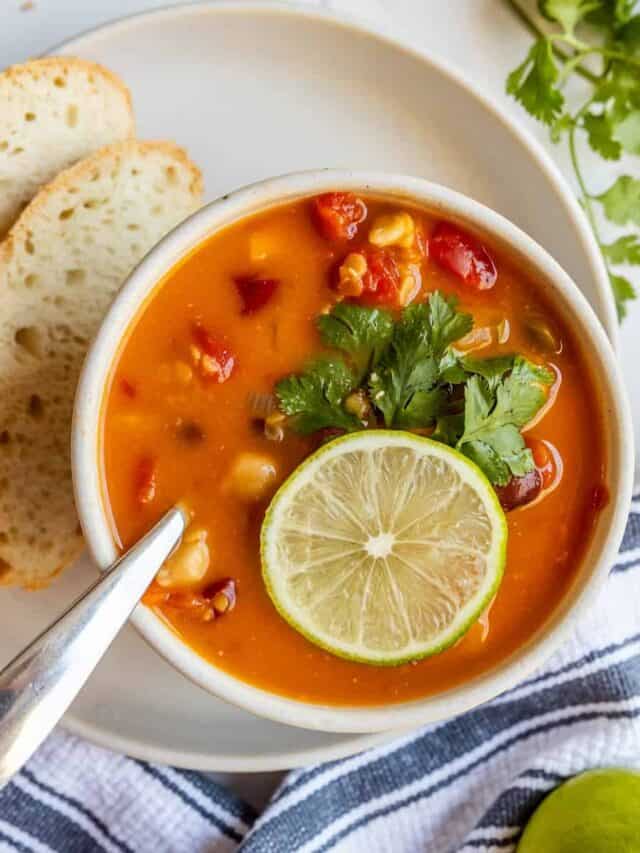 A bowl of vegetable soup garnished with lime and cilantro, served with slices of bread on the side.