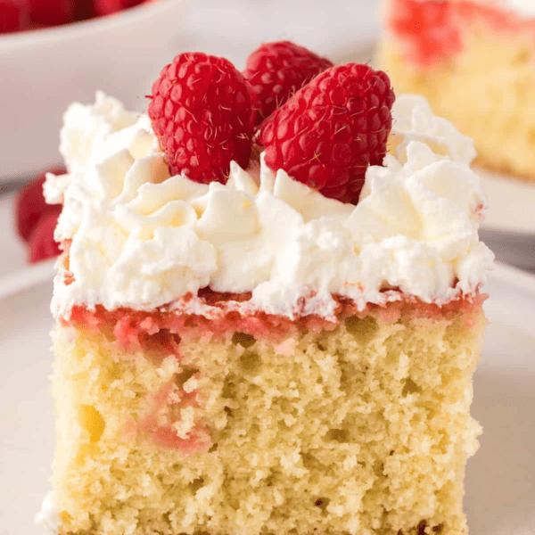 A slice of raspberry sheet cake topped with whipped cream and raspberries.