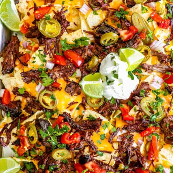 Platter of loaded carne asada nachos topped with jalapeños, tomatoes, cheese, and sour cream.