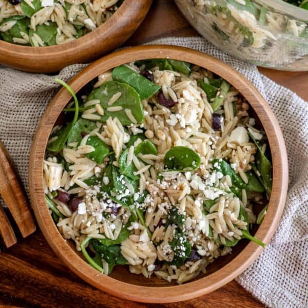 Two wooden bowls filled with spinach, feta, and orzo salad.