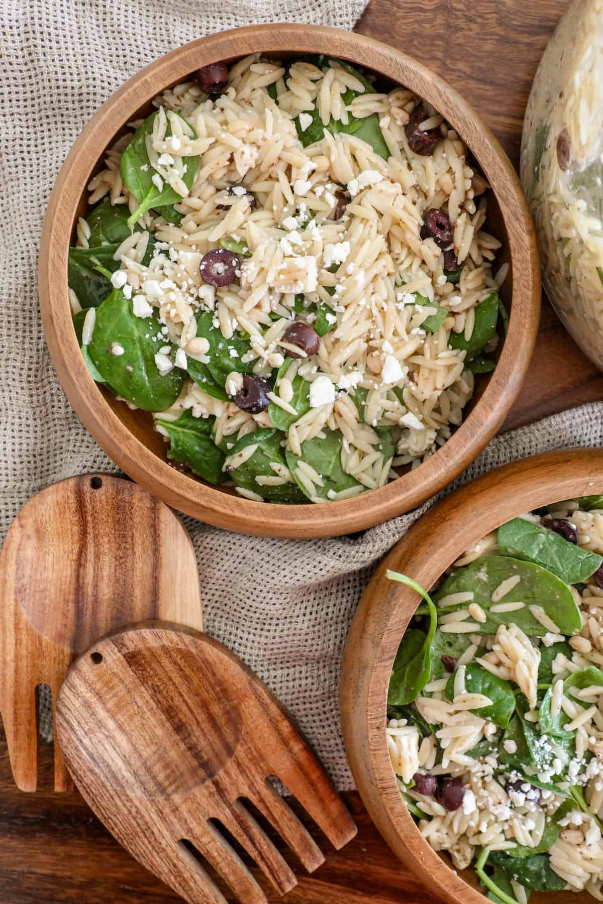 Two wooden bowls with spinach and orzo, one topped with feta.