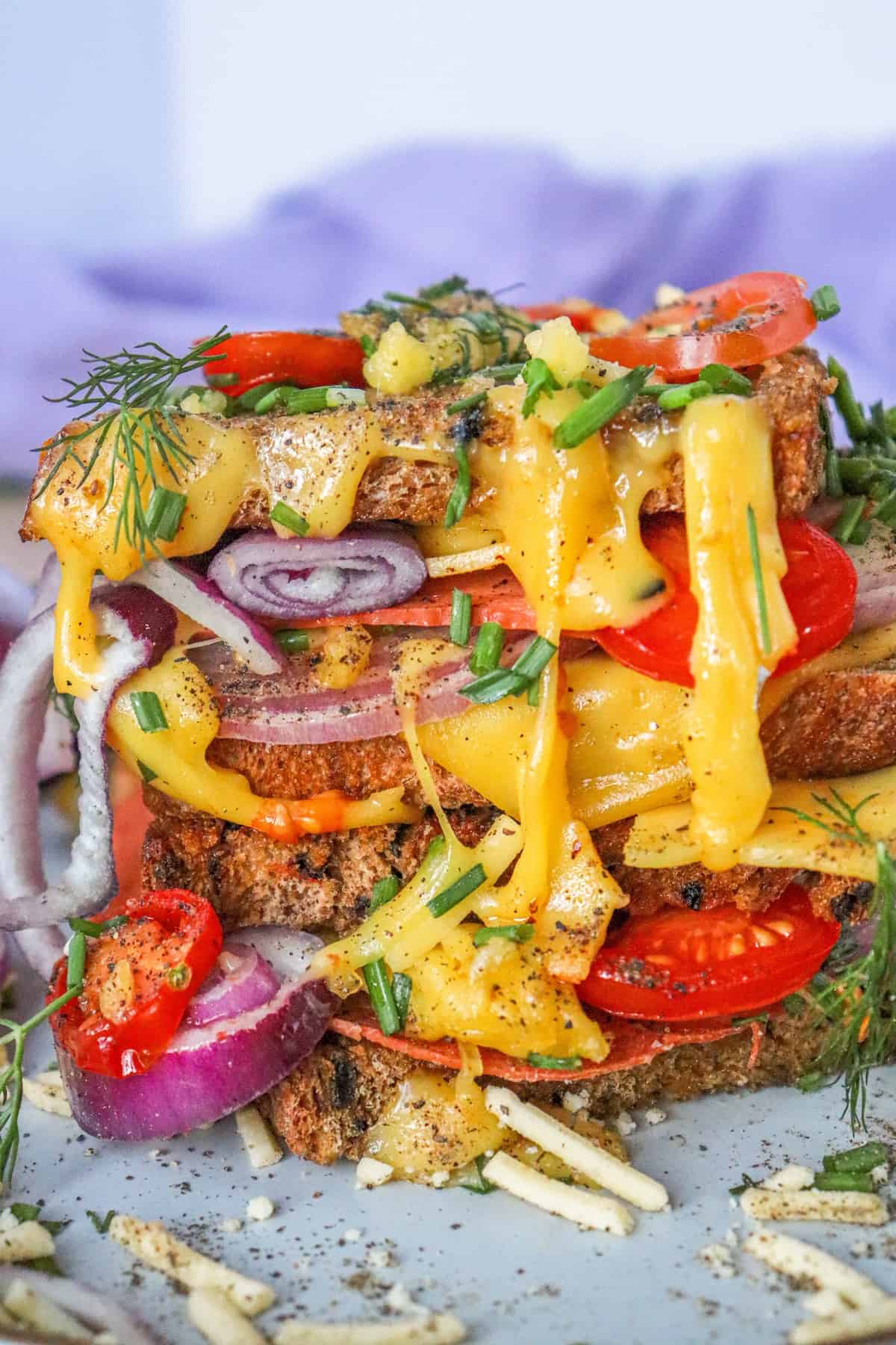 A stack of vegan sandwiches with melty cheese and tomatoes.