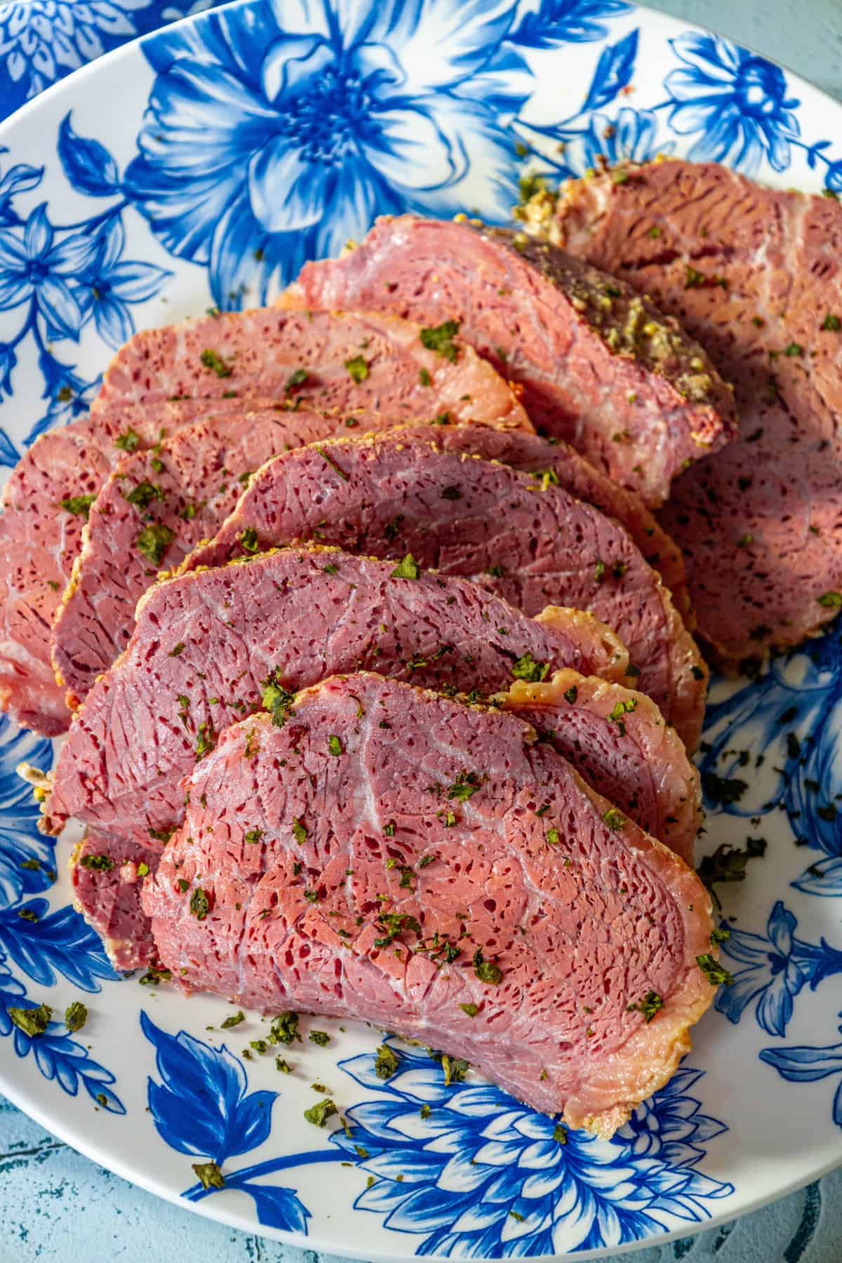 A plate of roasted corned beef on a blue and white floral pattern.