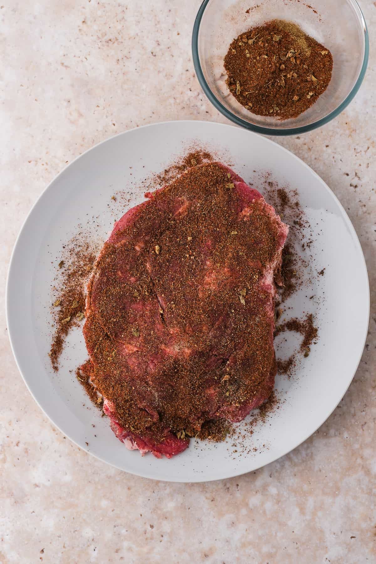 Raw shredded beef seasoned with dry spice rub on a white plate.