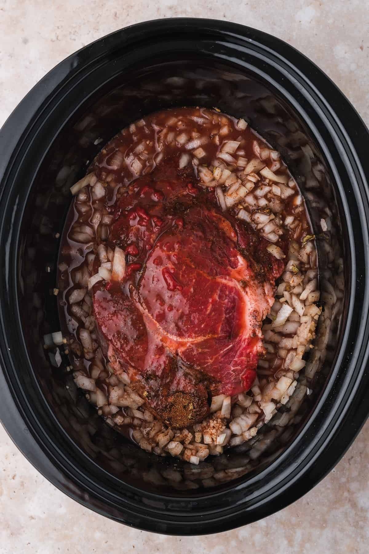 Beef tacos with shredded beef and chopped onions in a slow cooker, ready to cook.