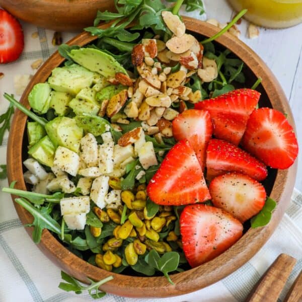 A bowl of salad with strawberries and avocado.