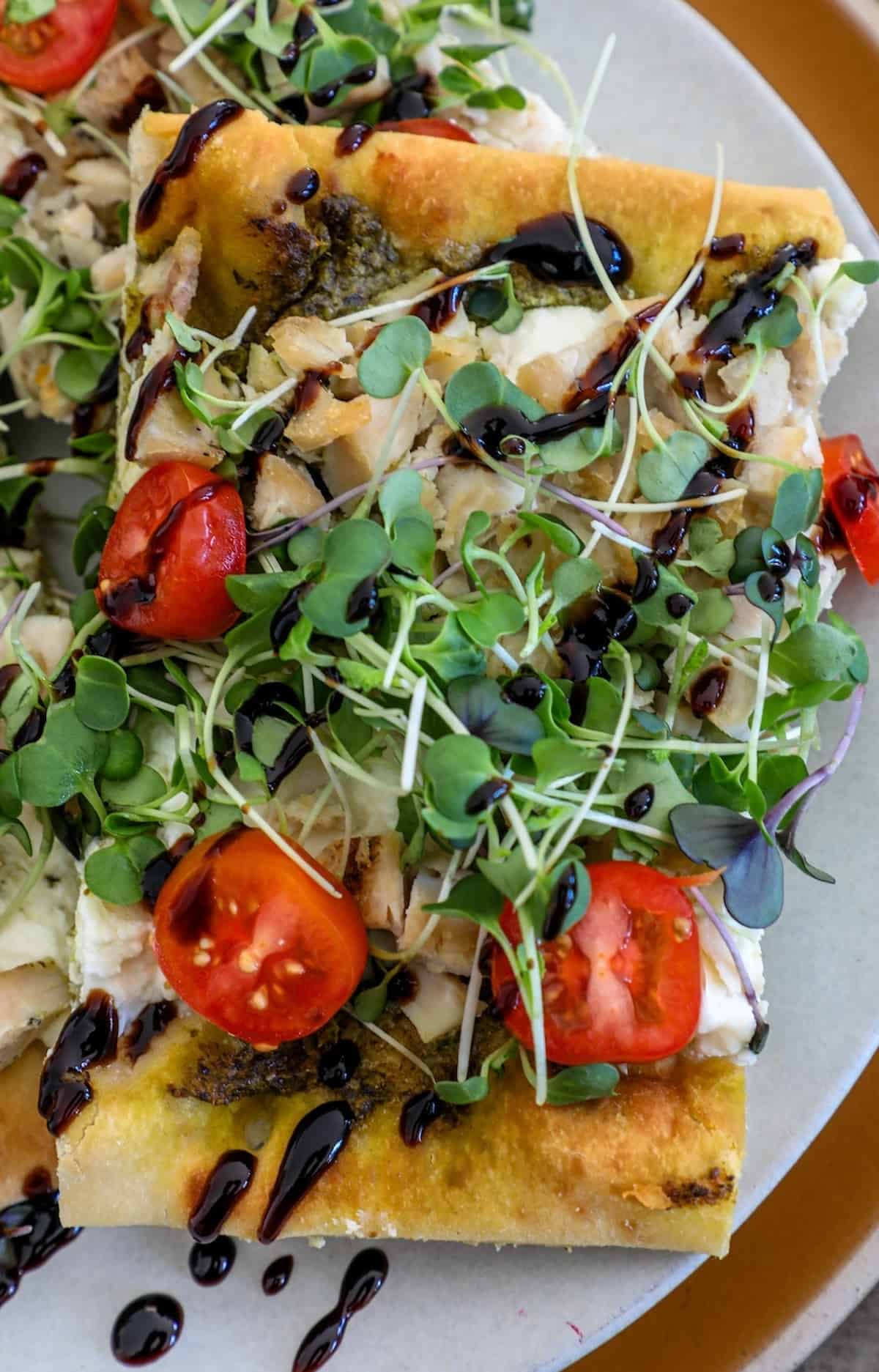 A flatbread pizza with tomatoes and greens on a plate.
