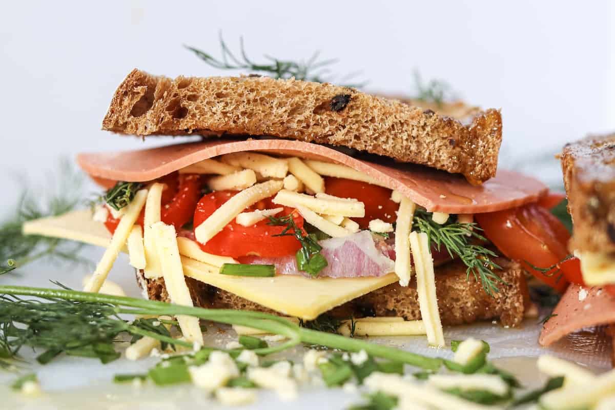 A vegan ham and cheese sandwich with tomatoes and dill.