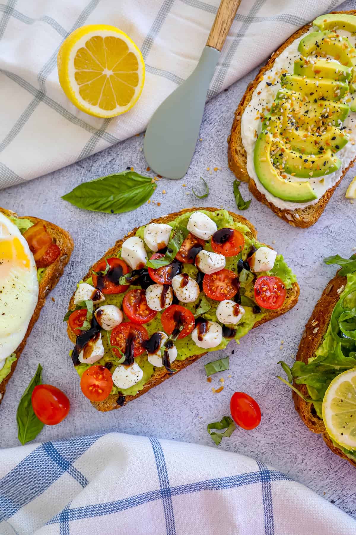 Four slices of toast with tomatoes, avocado, eggs and lemons.