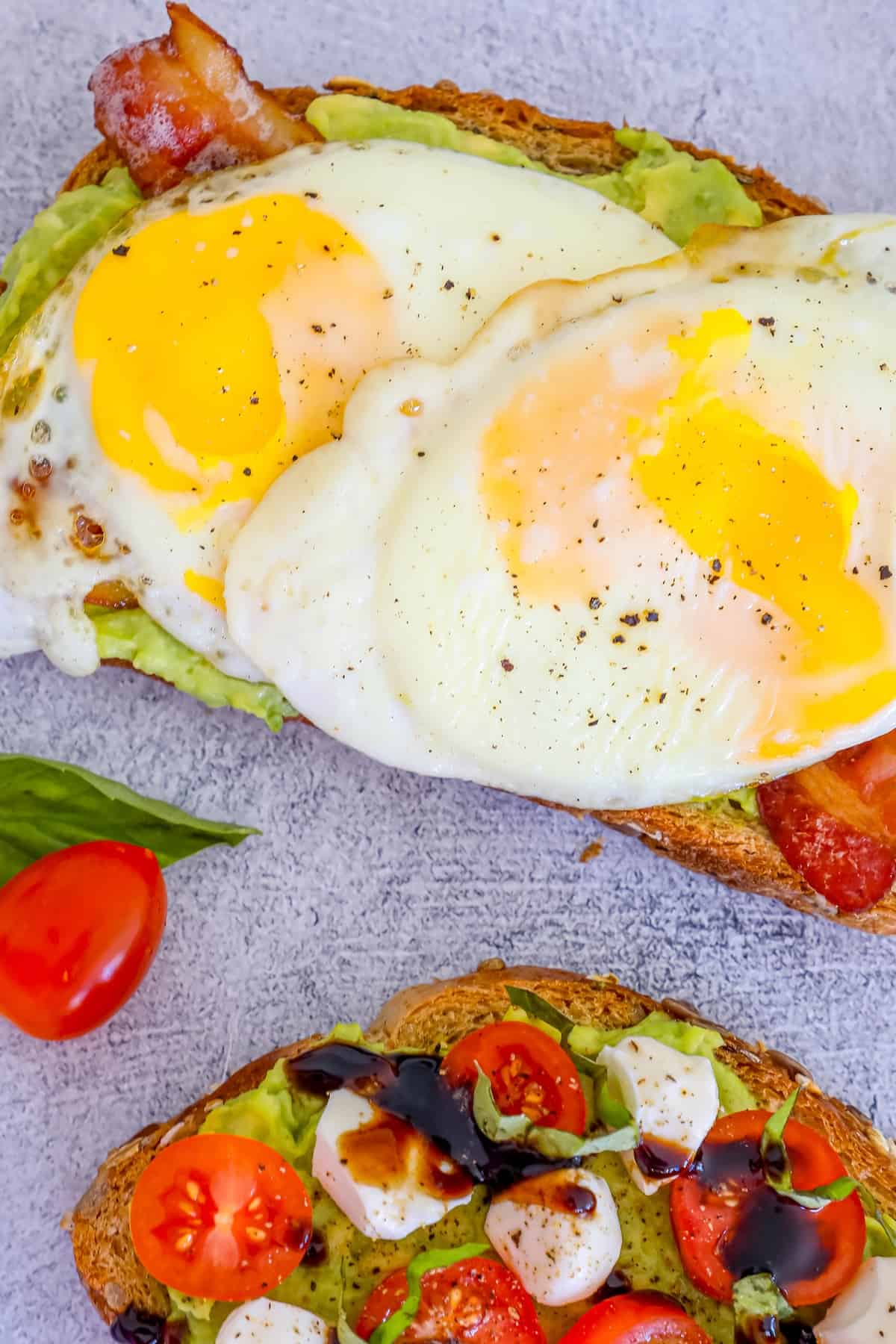 Two slices of toast with avocado, tomatoes and eggs.