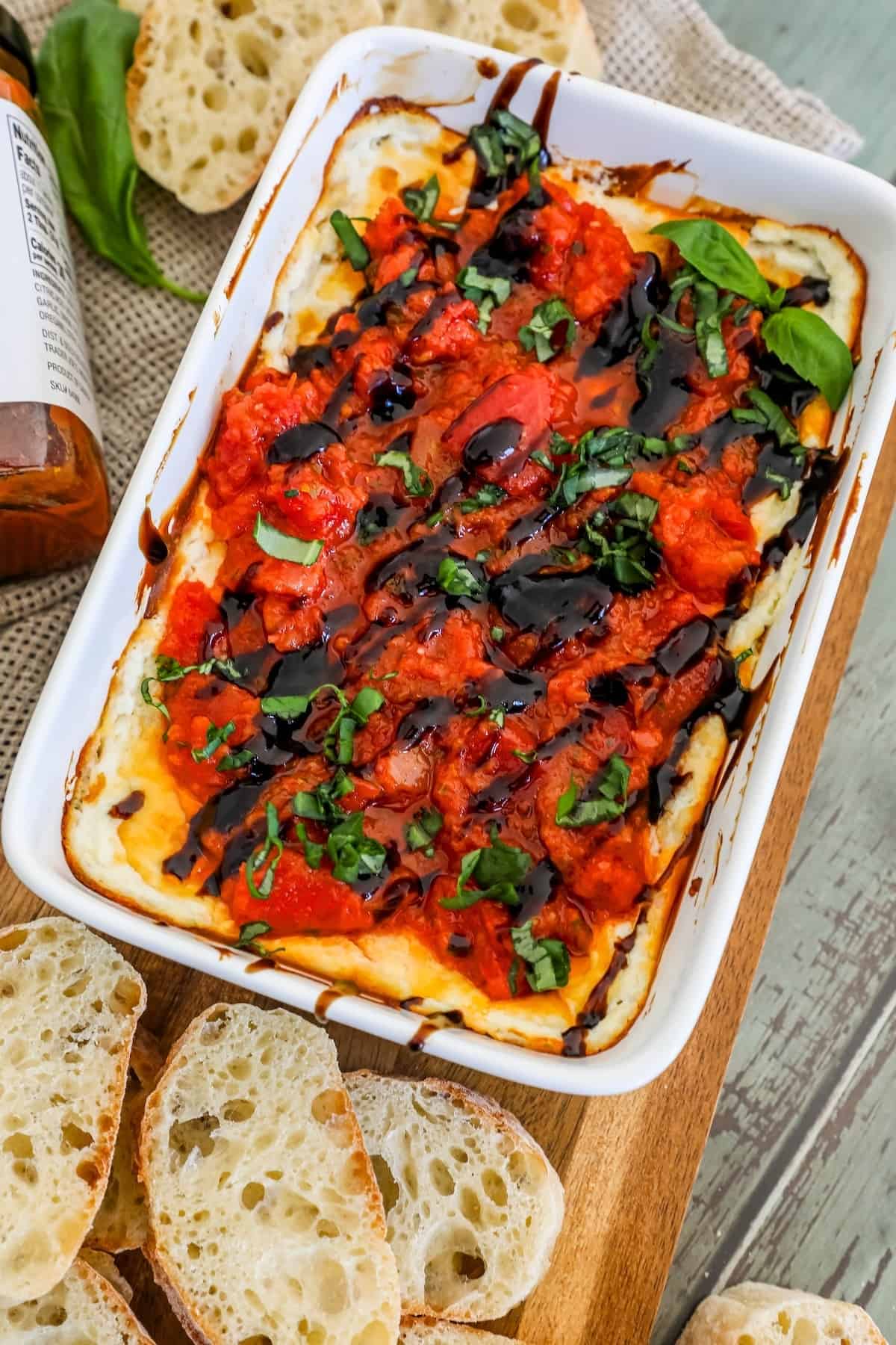 A dish of tomato and basil dip with bread on a cutting board, perfect for appetizing.