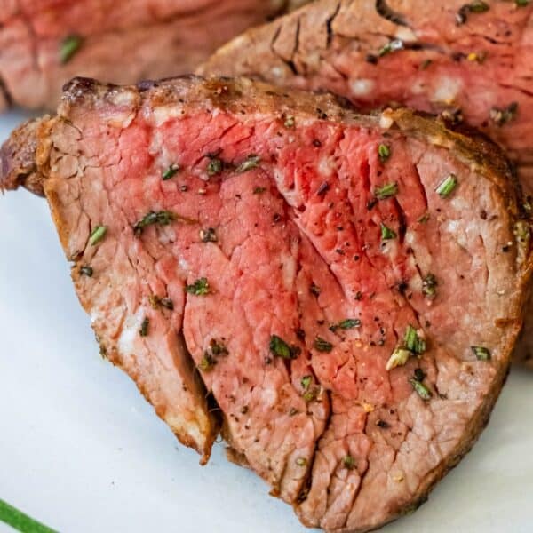 Close-up of a sliced, medium-rare beef tenderloin garnished with herbs and pepper.