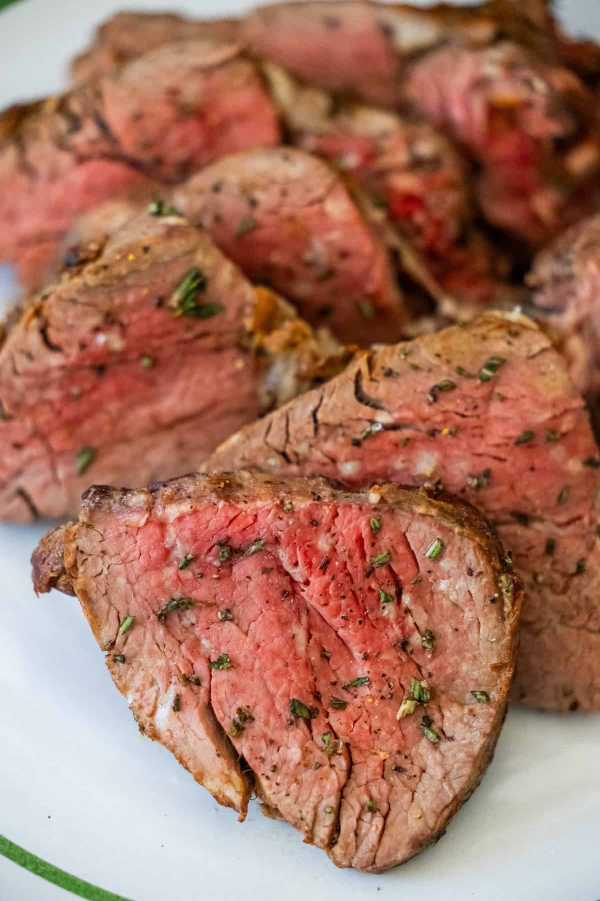 Sliced medium-rare beef tenderloin with herbs elegantly presented on a white plate.