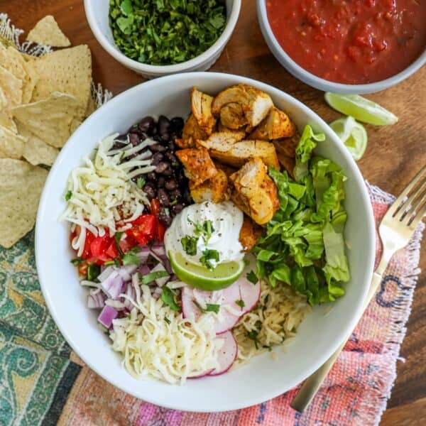 A bowl of chicken burrito bowls with assorted toppings and a side of tortilla chips.