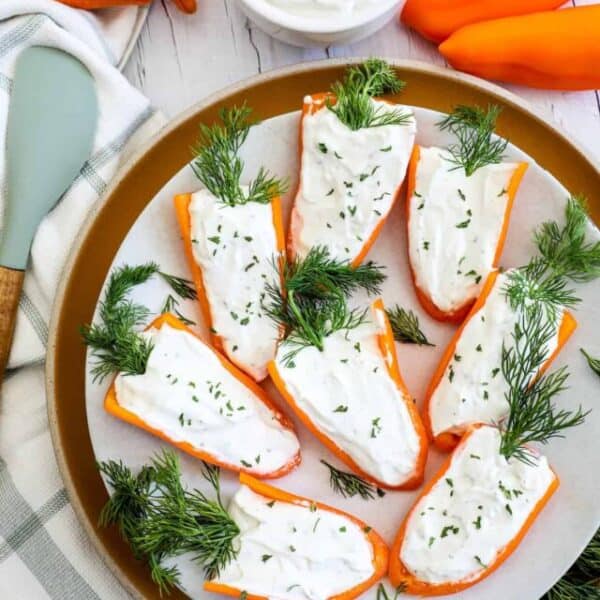 Sliced carrots topped with a white creamy sauce and garnished with fresh dill on a beige plate.