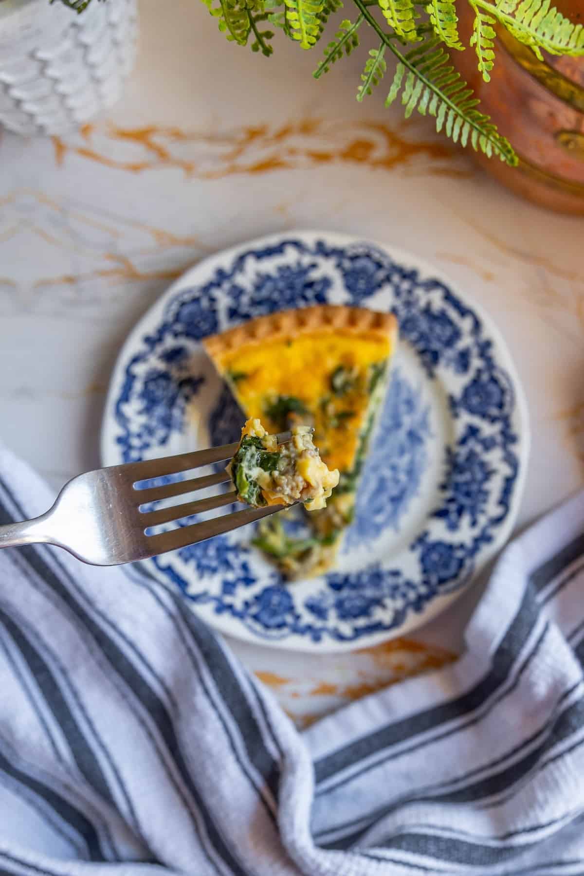 A quiche slice on a plate with a fork.