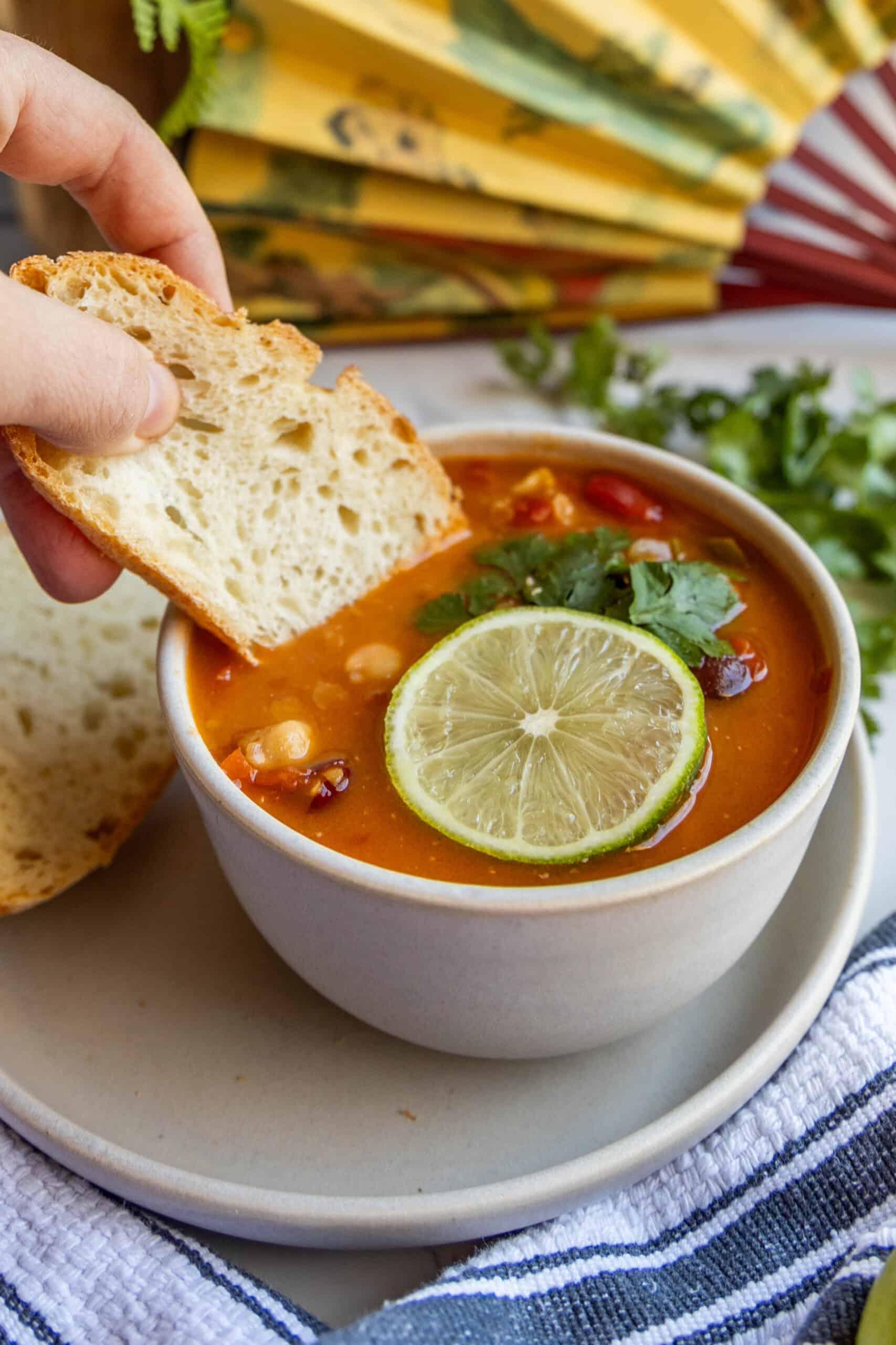 A person is dipping bread into a bowl of soup with a Thai chili.