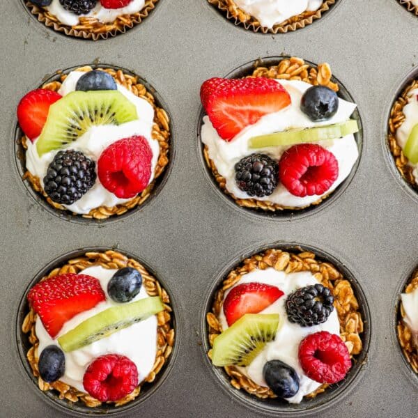 Granola fruit cups filled with yogurt and topped with mixed fresh fruits including strawberries, blueberries, blackberries, raspberries, and kiwi slices.