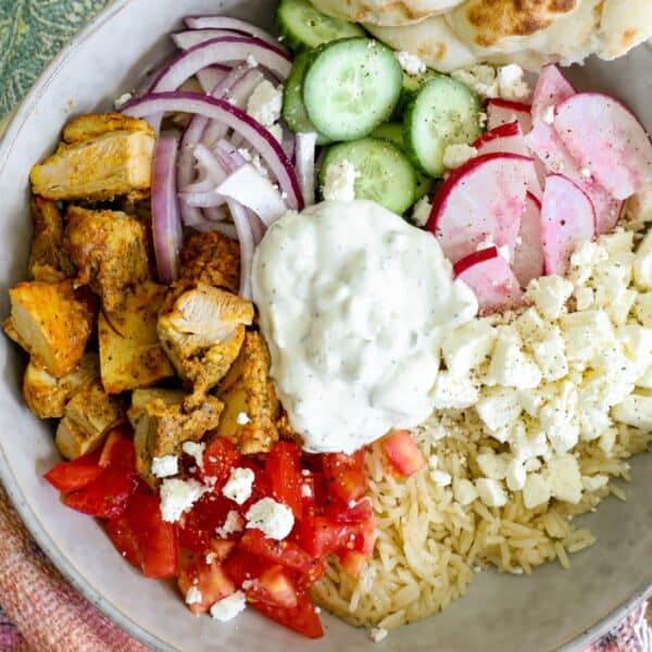 A bowl of greek chicken gyros with rice, tomatoes, cucumbers, red onions, feta cheese, and tzatziki sauce.
