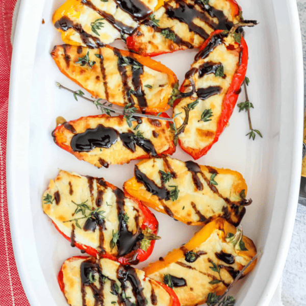 Baked peppers in a white dish with black olives and thyme.
