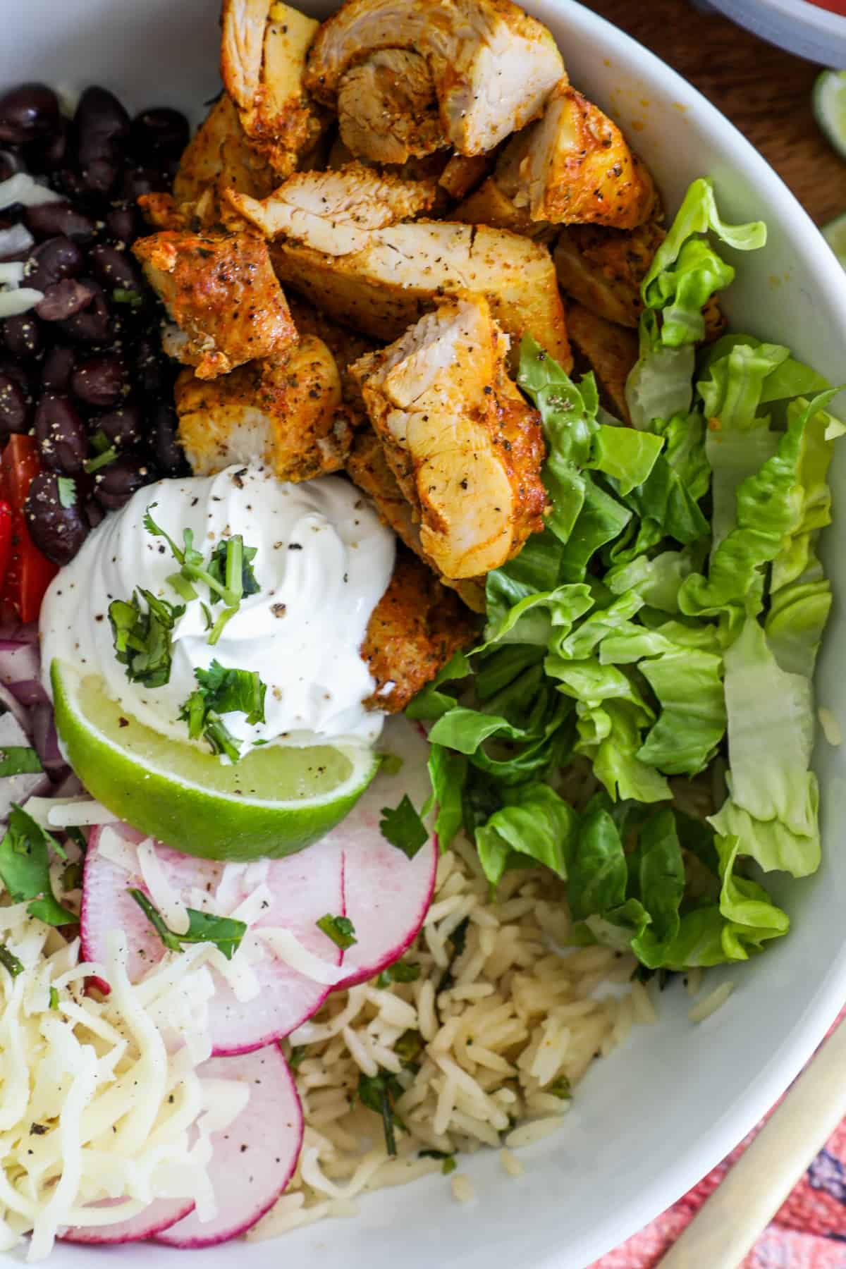 chicken, lettuce, black beans, tomatoes, lime, and sour cream in a bowl