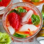 A close-up of a strawberry mojito drink with fresh strawberries, mint leaves, ice, and lime slices in a glass.