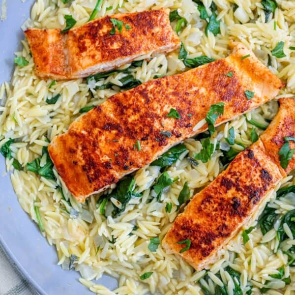 Three pieces of grilled salmon on a bed of orzo and spinach, served on a blue plate.