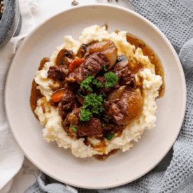 A plate of beef bourguignon served over mashed potatoes, garnished with parsley.