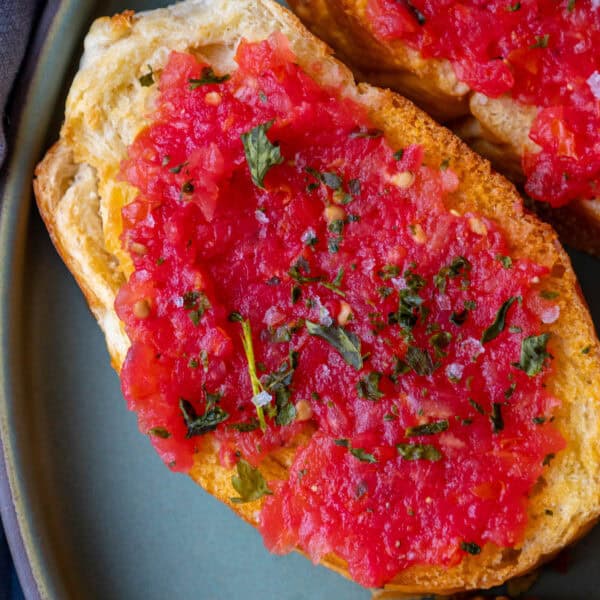 Two slices of bread topped with finely chopped tomatoes and herbs on a plate, this Pan Con Tomate is a classic Spanish recipe.