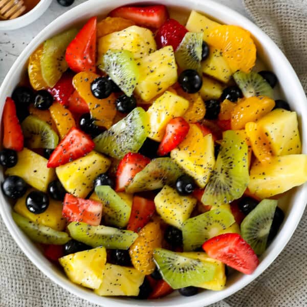 A bowl filled with a variety of fresh fruit chunks: pineapple, strawberries, kiwi, mandarin oranges, and blueberries, sprinkled with small seeds. Truly the best fresh fruit salad you can enjoy!