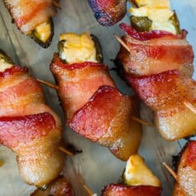 Bacon-wrapped, cheese-stuffed jalapeños are arranged on a metal baking sheet, secured with toothpicks.