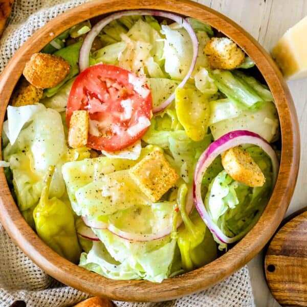 A wooden bowl filled with a salad featuring lettuce, a slice of tomato, red onion rings, croutons, and dressing.