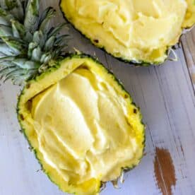 A halved pineapple filled with smooth, creamy pineapple dessert on a wooden surface.