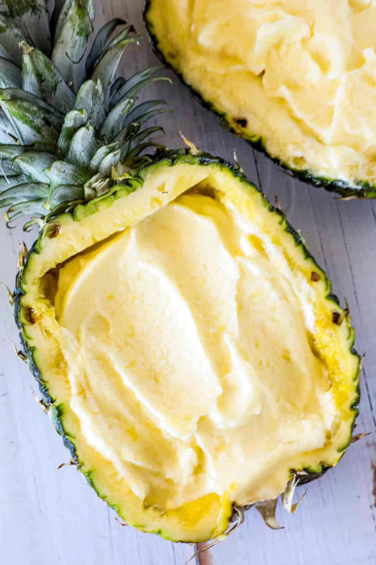 A halved pineapple filled with smooth, creamy yellow ice cream against a light background.