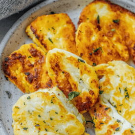 A plate of Easy Pan Fried Halloumi Greek Cheese, golden brown and garnished with chopped herbs.