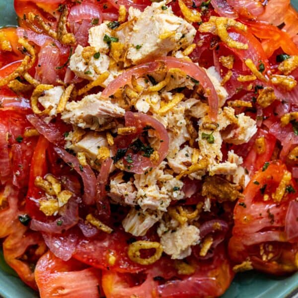 Close-up of a Tomato Salad featuring slices of tomatoes topped with shredded cooked chicken, caramelized onions, and crispy fried onions.